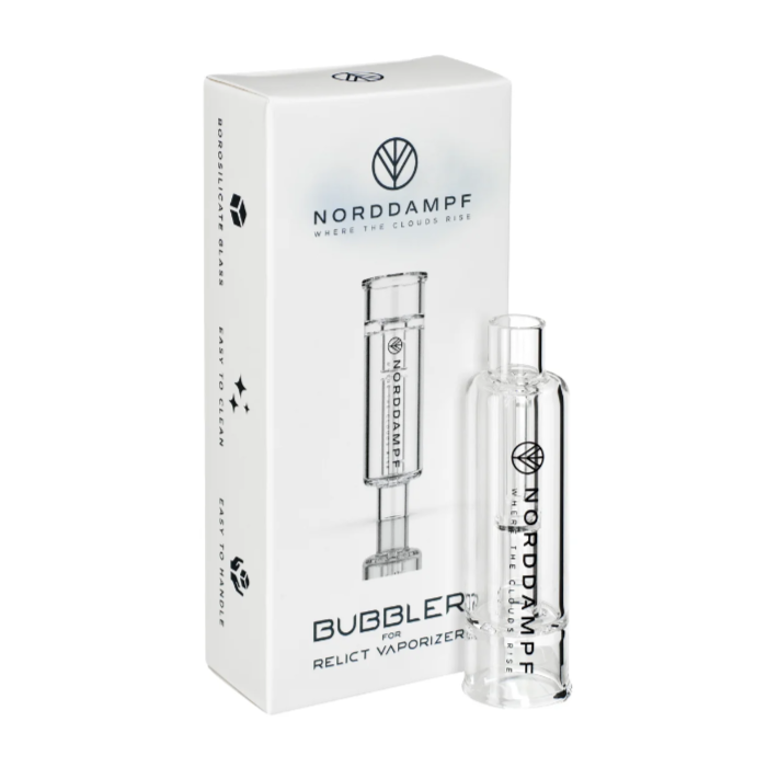 Auf dem Bild ist in Hintergrund die Originalverpackung des Bubbler/ Wasserfilter für den Norddampf Relict Kräuter Verdampfers zu sehen. Im Vordergrund steht der Wasserfilter aufrecht. Die Farbe des Glases ist transparent. Es handelt sich um ein Originales Zubehör für den Norddampf Relict Vaporizer.